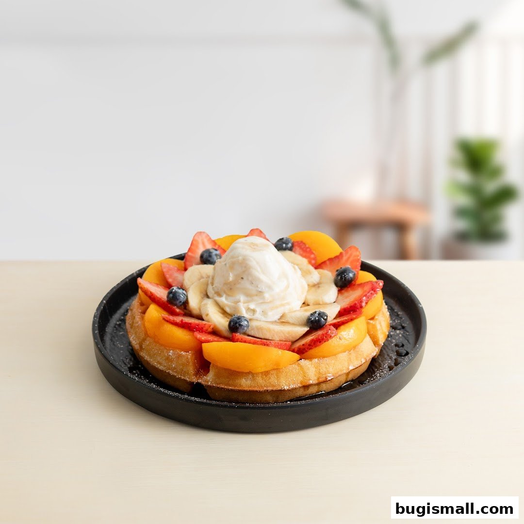 A delicious waffle topped with ice cream and fresh fruits like strawberries, blueberries, peaches, and bananas.