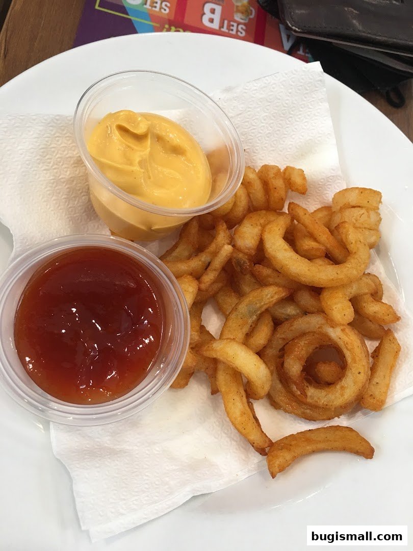 A plate of curly fries served with ketchup and cheese dip on a white napkin.