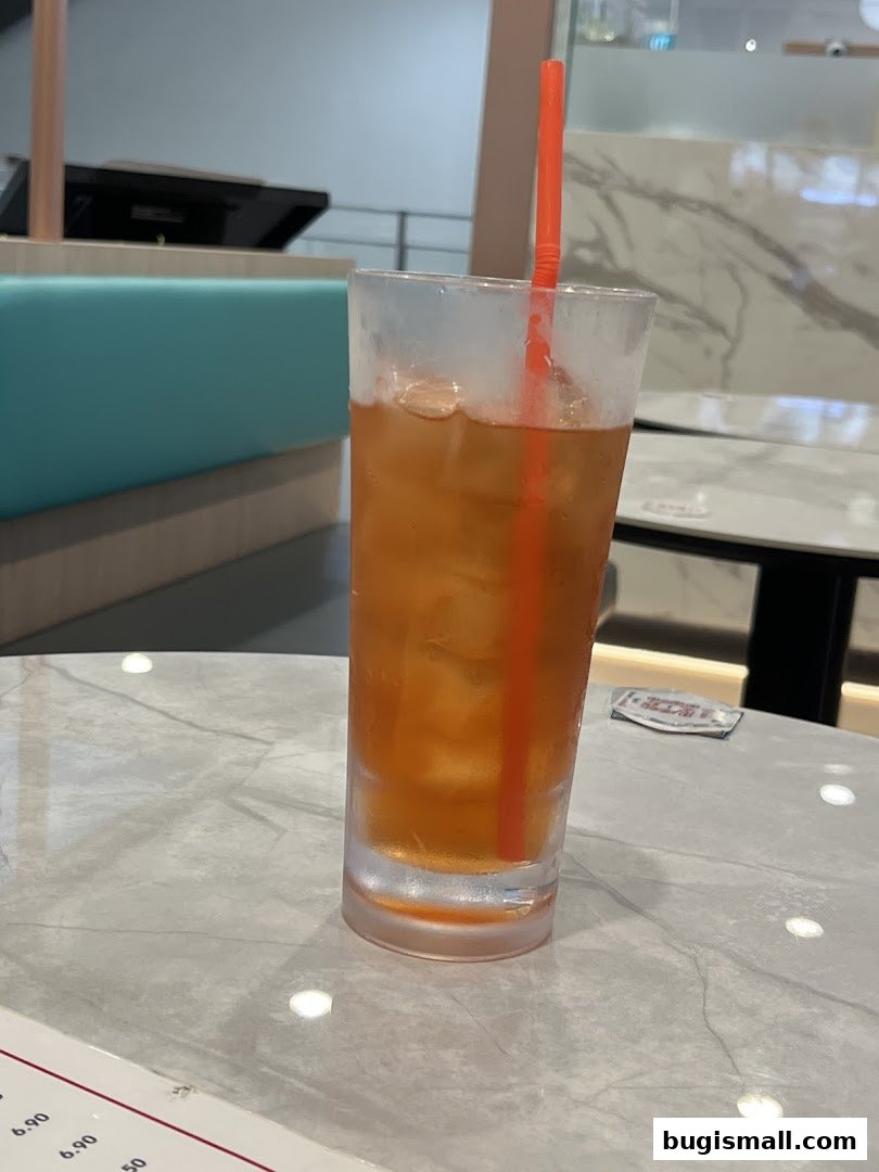 A tall glass of iced tea with an orange straw sits on a marble table.