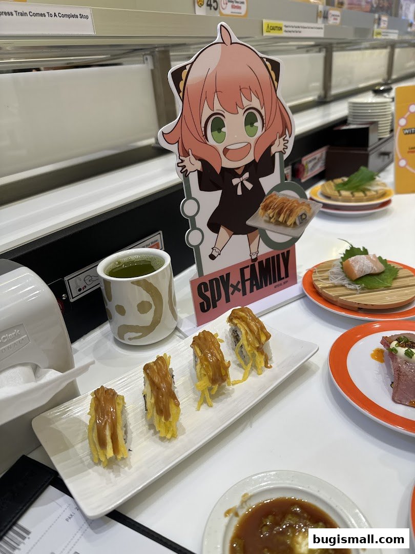 A table at Genki Sushi with sushi, green tea, and a Spy x Family cutout.