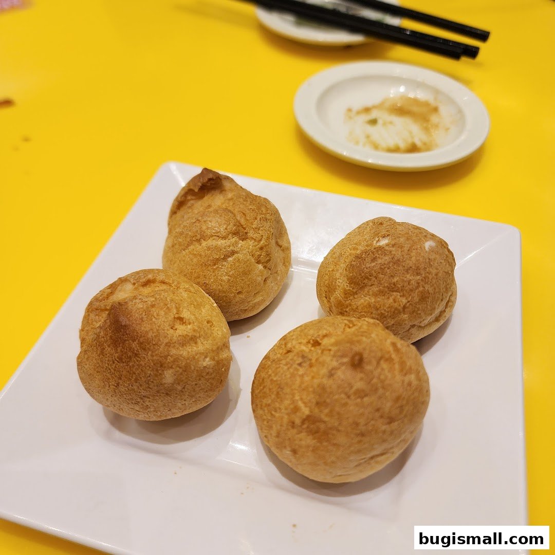 Four golden-brown cream puffs served on a white square plate with chopsticks in the background.
