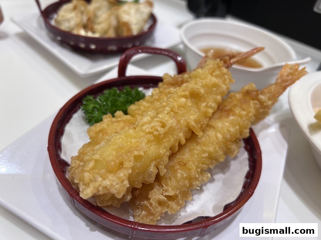 Crispy tempura shrimp served in a basket with dipping sauce and gyoza in the background.