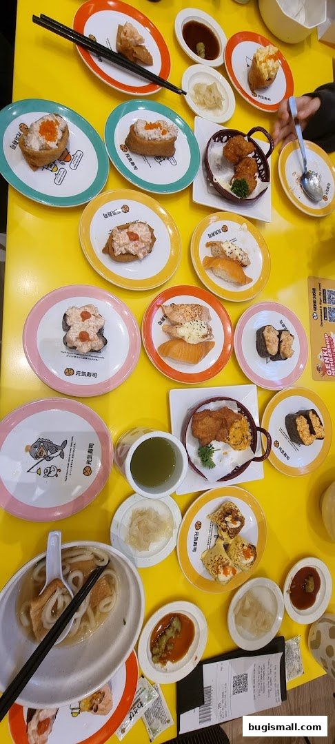 A table full of various sushi dishes, udon soup, and drinks at Genki Sushi.
