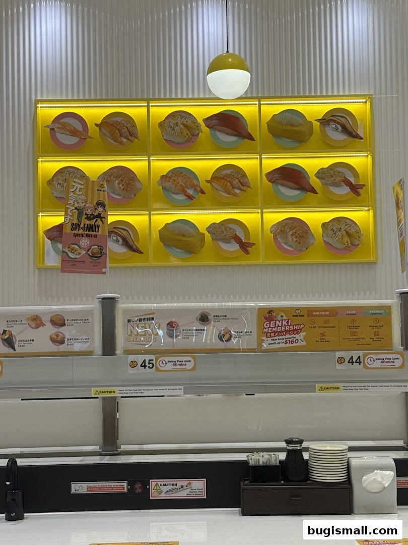 A display of sushi dishes on a yellow illuminated wall at Genki Sushi.