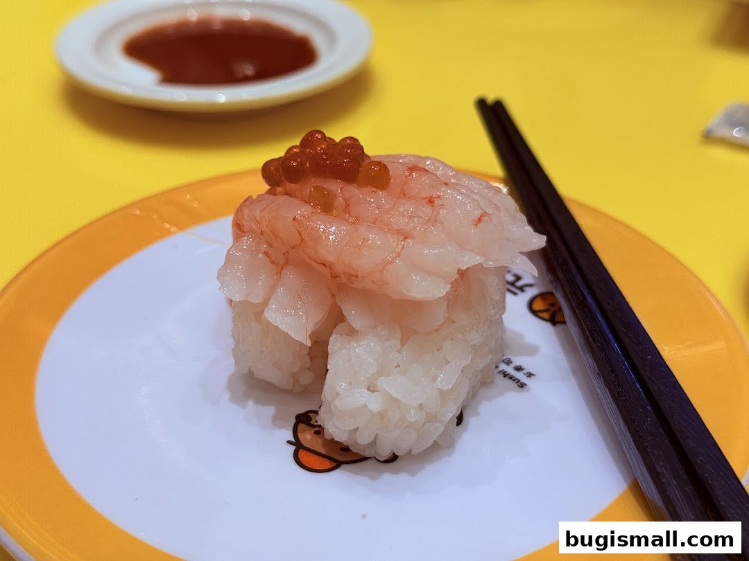 A close-up of a sushi dish with shrimp and roe, served with chopsticks and dipping sauce.