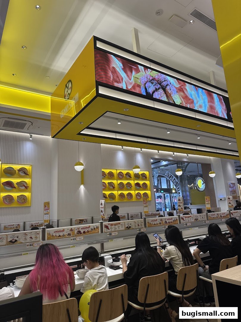 Interior of Genki Sushi Bugis with customers seated at a conveyor belt sushi bar.