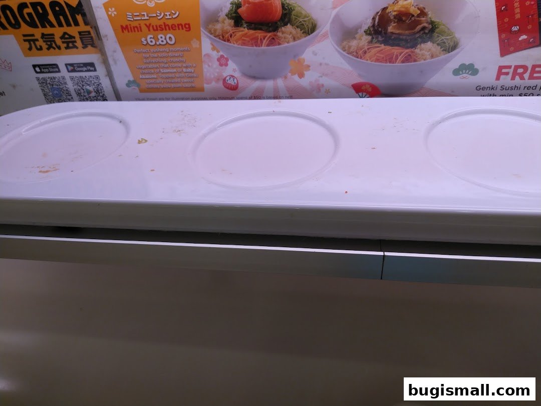 A close-up of a conveyor belt sushi display with a menu item for Mini Yusheng.