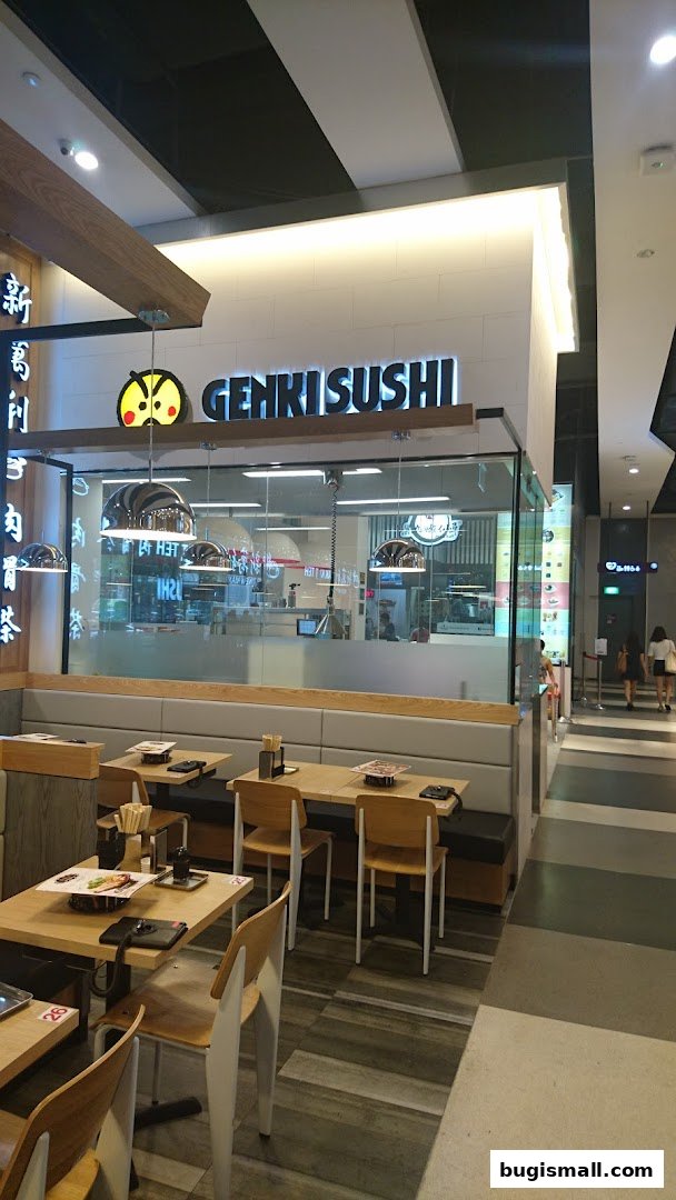 Interior view of Genki Sushi Bugis with tables, chairs, and the restaurant's signage.