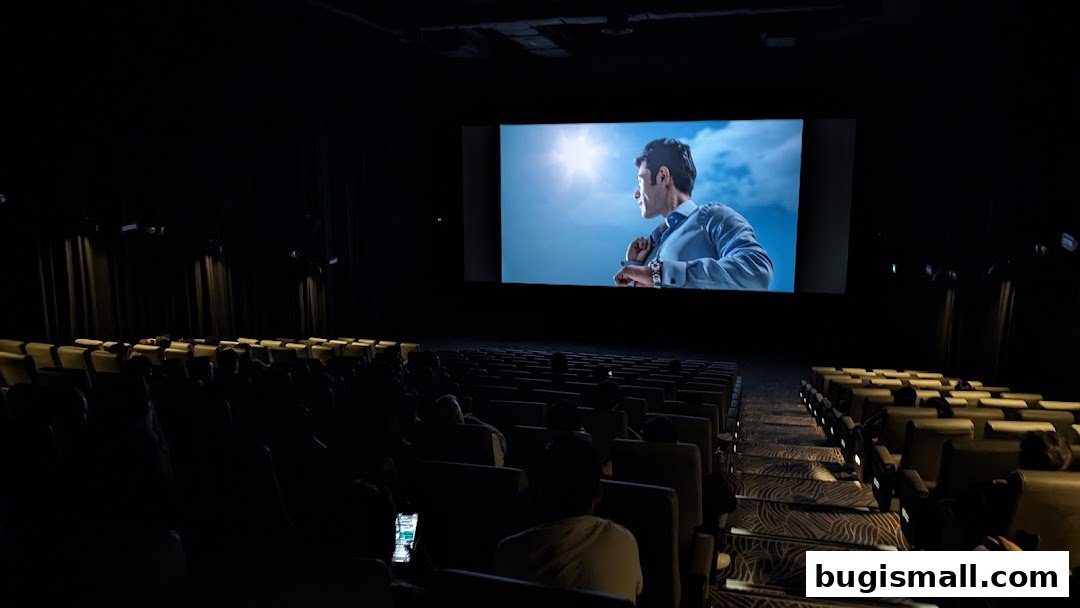 An audience watches a movie on a large screen in a darkened cinema hall.