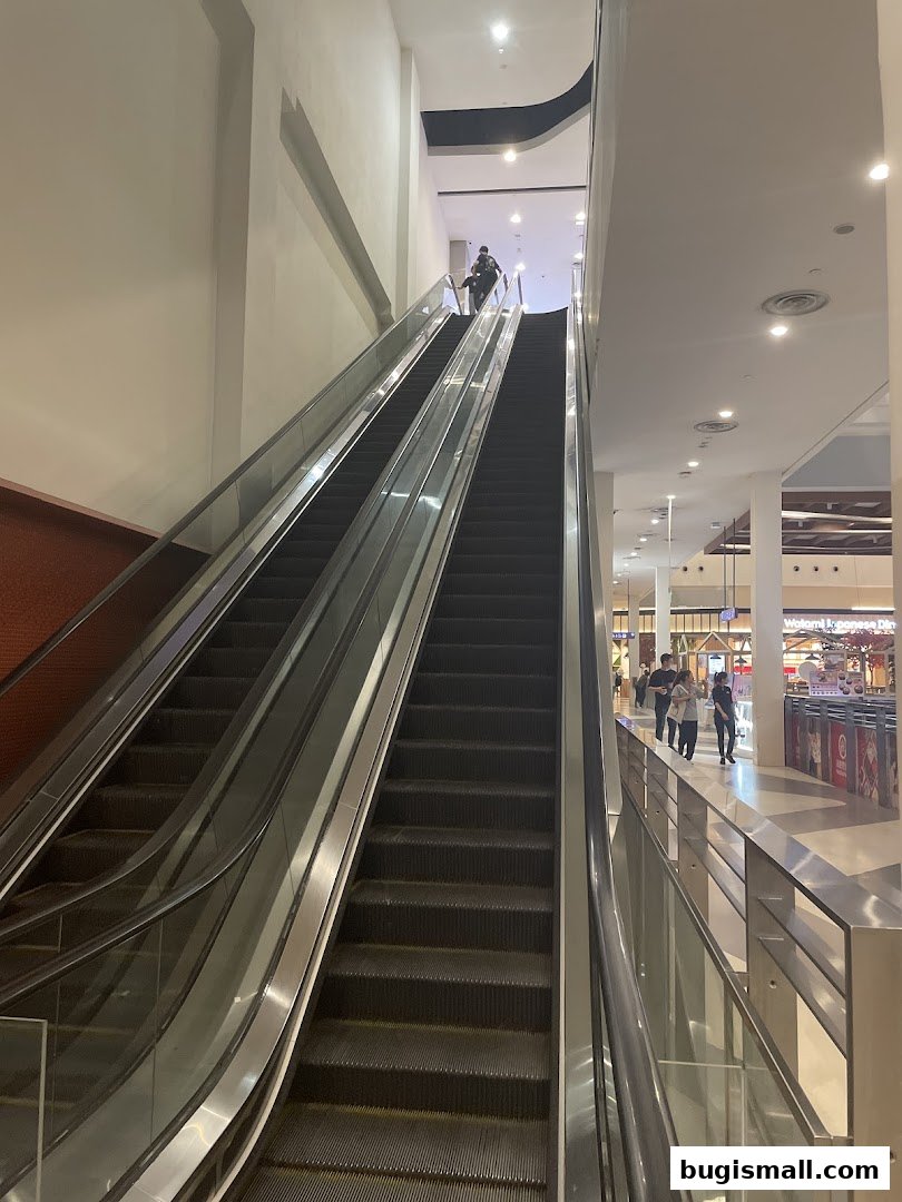 Escalators in a modern shopping mall with people walking on them.