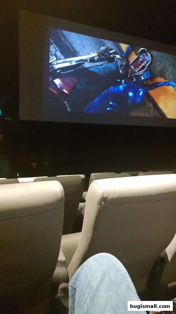 A person's legs in jeans in a cinema seat, watching a movie on screen.
