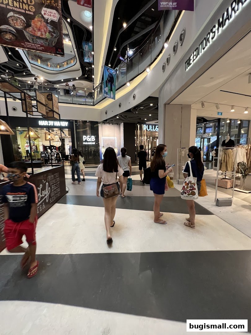 People walking in a modern shopping mall with various shop fronts visible.