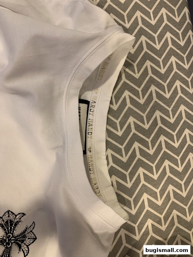 Close-up of a white t-shirt with a prominent cross design and brand labeling.