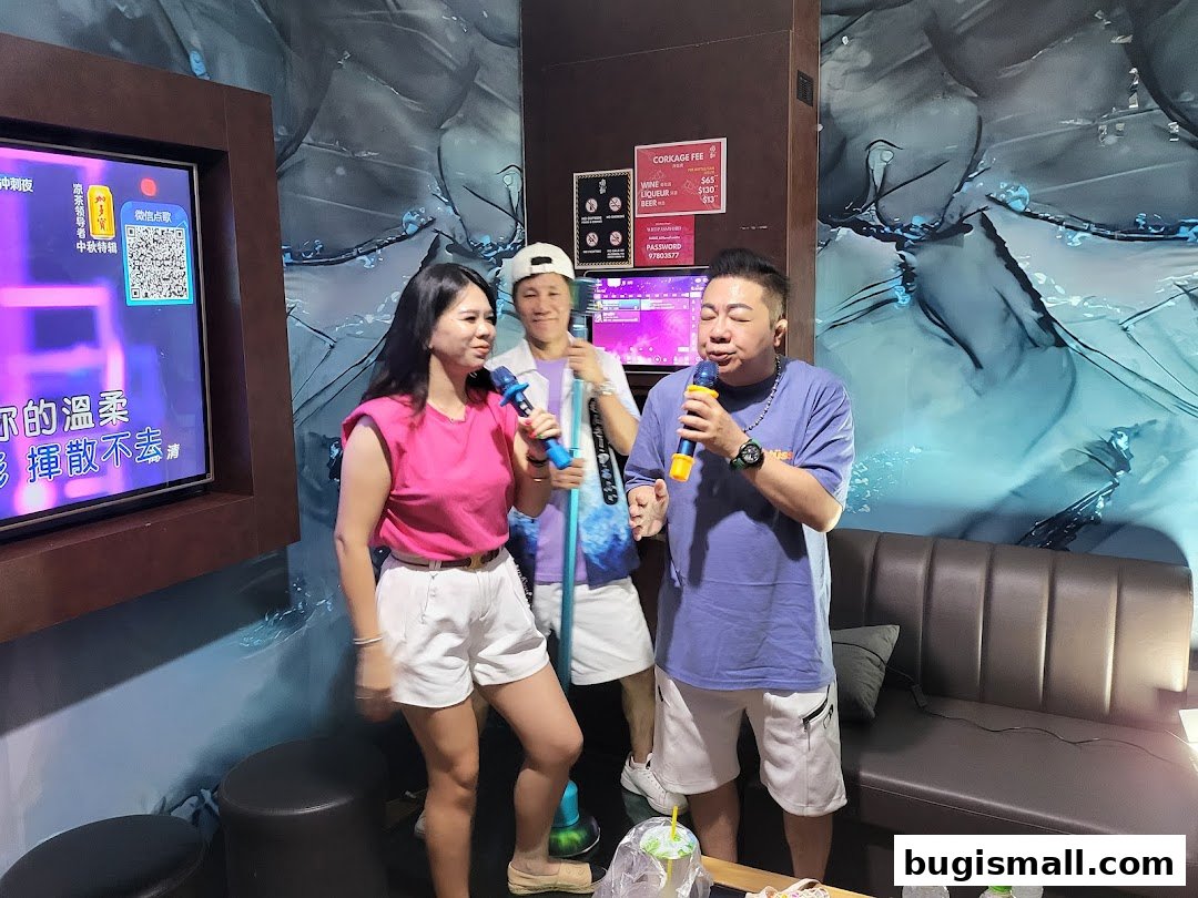 Three people are singing karaoke in a room with a large screen and a sofa.