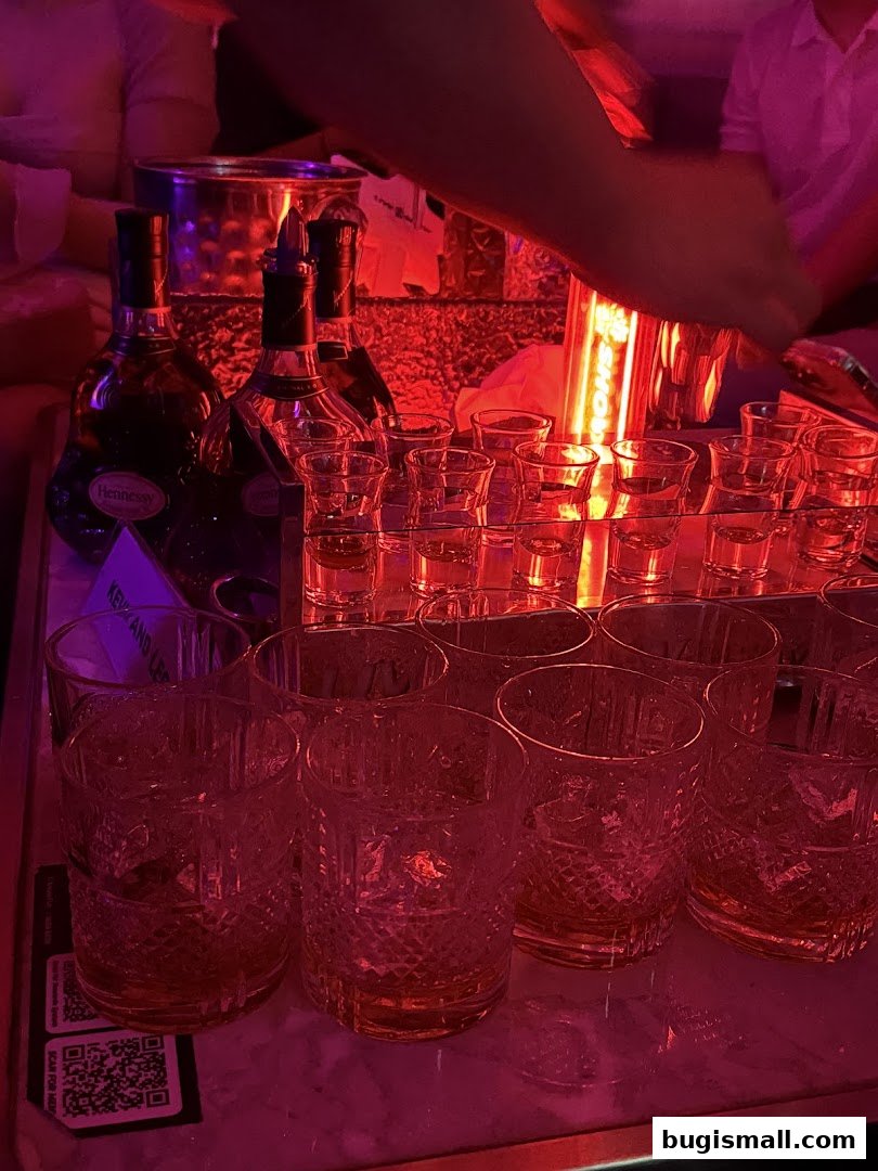 Bottles of Hennessy and shot glasses are arranged on a bar with red lighting.
