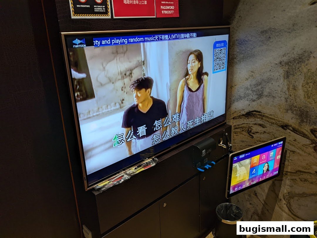 A karaoke screen displaying a music video with lyrics and a tablet for song selection.