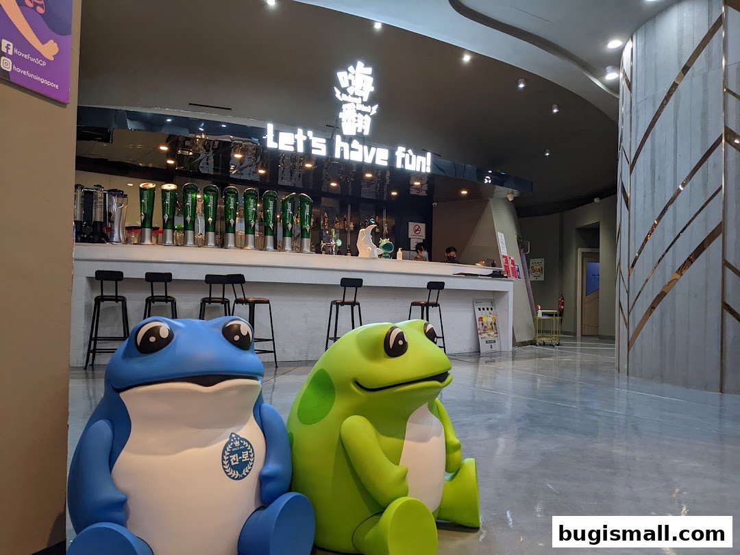Two large frog mascots sit in front of a bar area with beer taps and a counter.