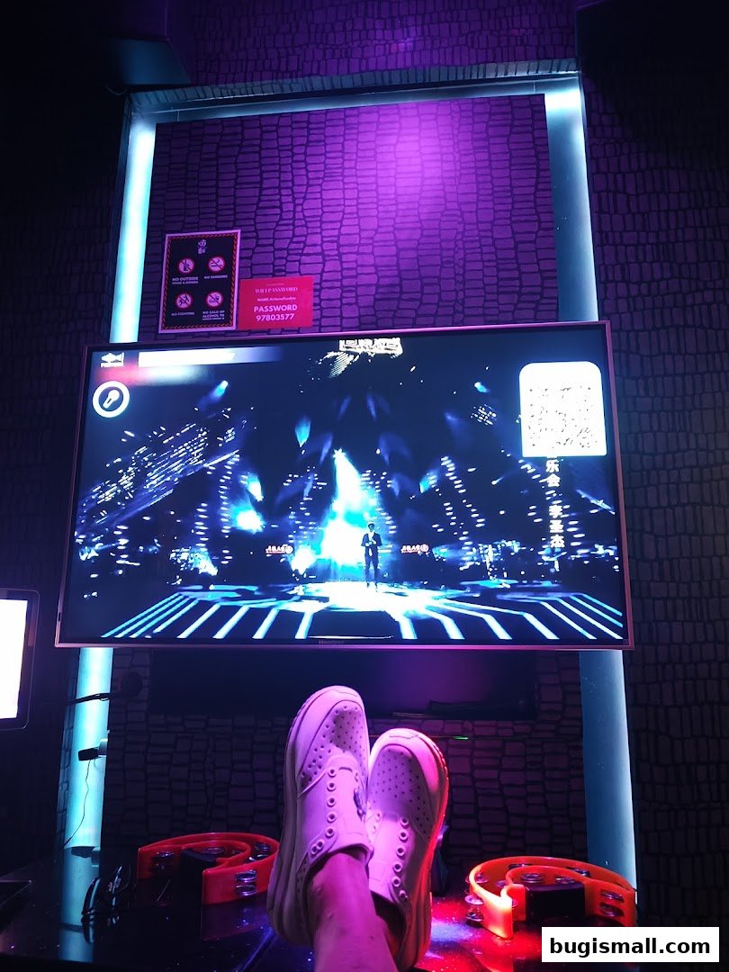 A person's feet in white shoes rest in front of a large screen displaying a concert.