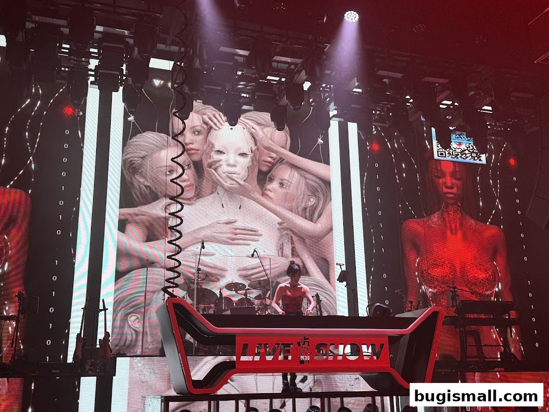 A DJ performs on stage with a large screen displaying artistic visuals and binary code.