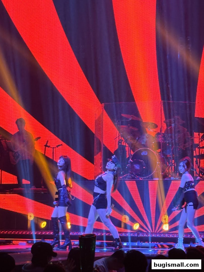 Performers on stage with a vibrant red and black backdrop and stage lighting.