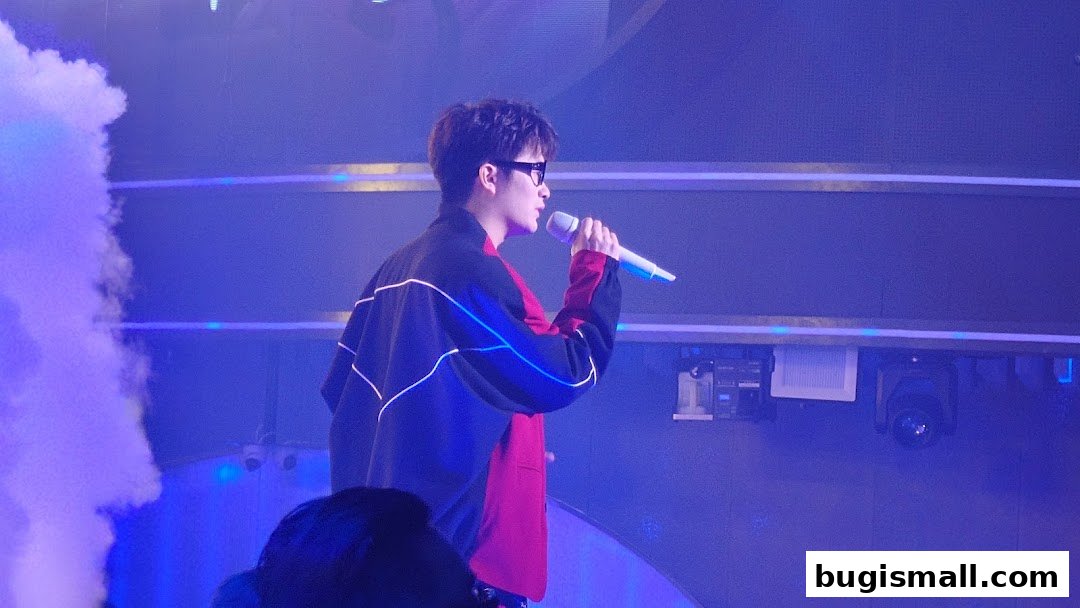 A performer sings into a microphone on a stage with blue lighting and smoke.