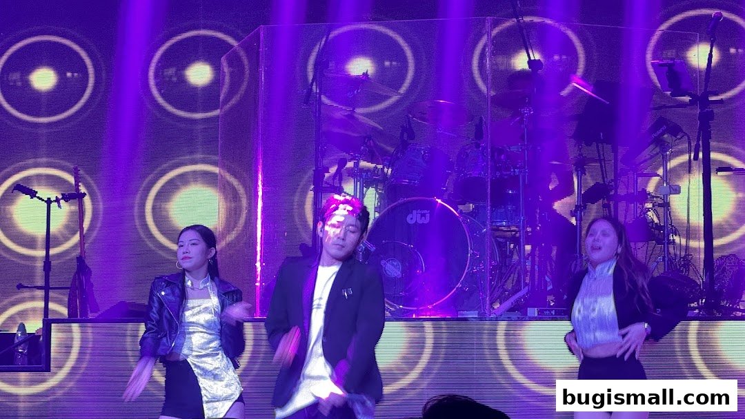 Performers dancing on stage with a drum set and purple lighting.
