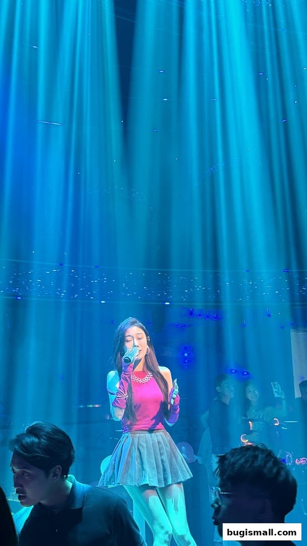 A female singer performs on stage under blue spotlights, with an audience watching.