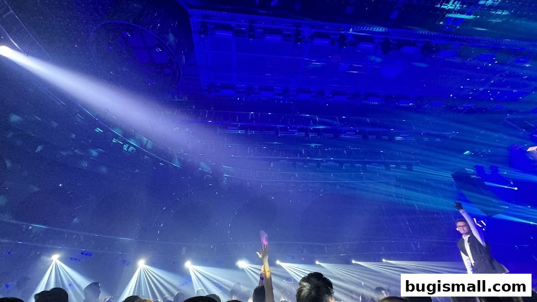A performer on stage with a crowd watching under blue spotlights and stage lighting.