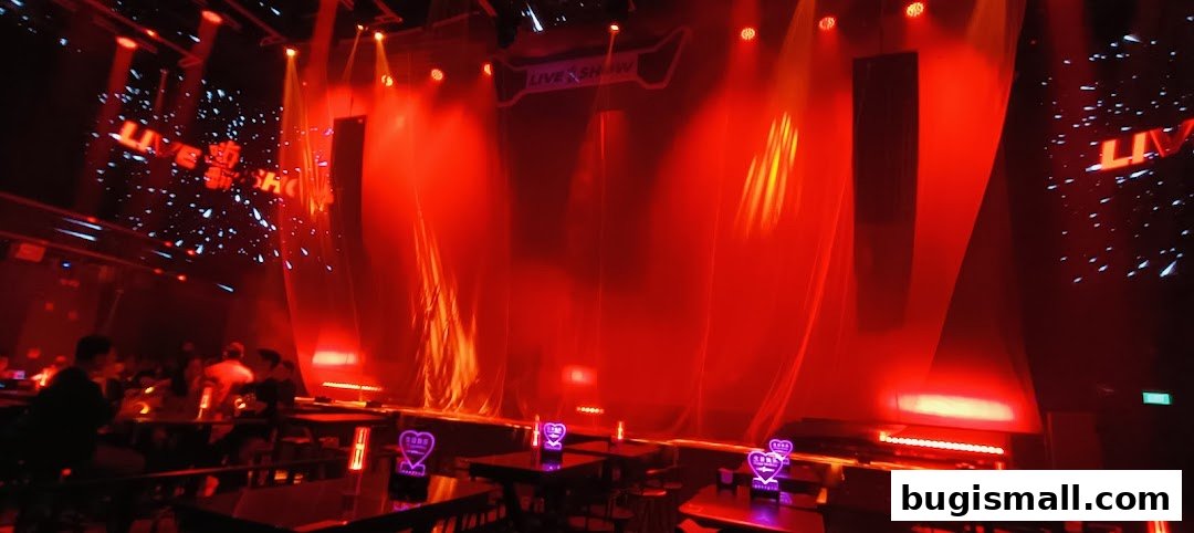 A dimly lit venue with a stage, red lighting, and tables with patrons.