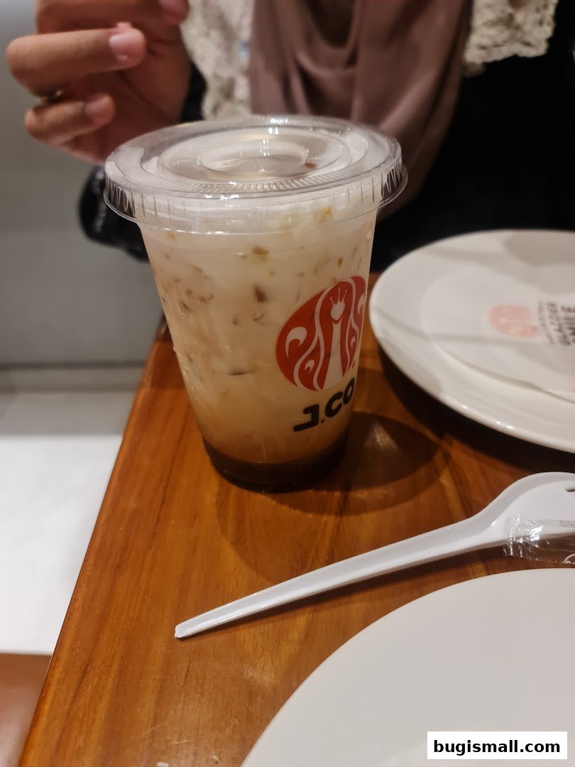 A close-up of a J.CO Donuts & Coffee iced beverage with a plastic fork on a wooden table.