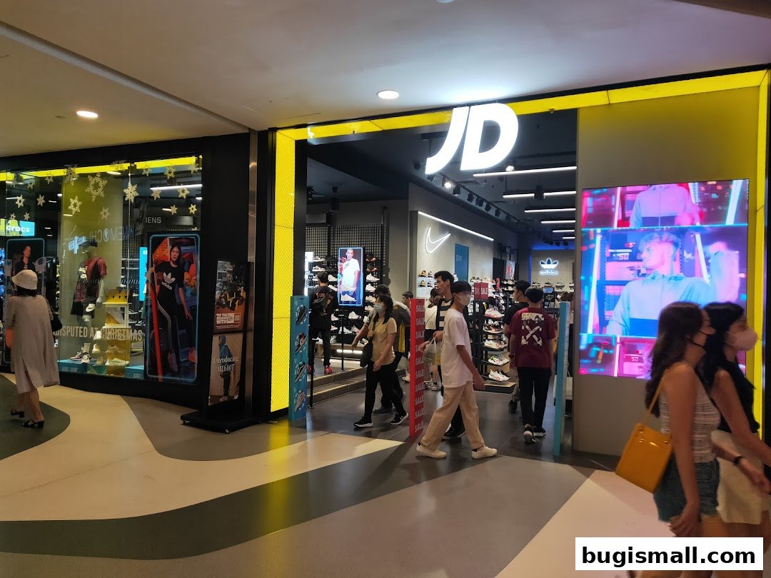 JD Sports store entrance with displays of athletic wear and shoes, and people walking by.