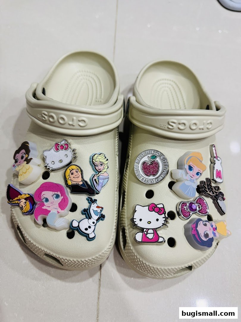 A pair of beige Crocs adorned with various character jibbitz, including Disney princesses and Hello Kitty.