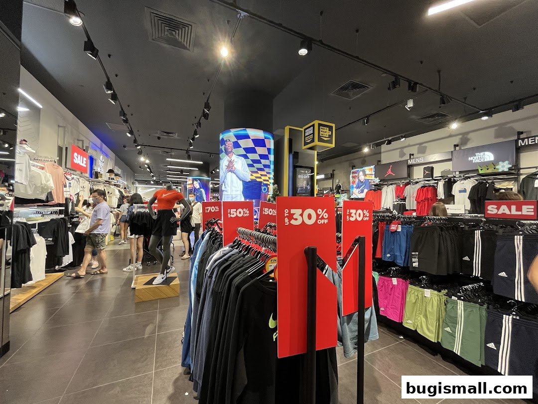 Interior of JD Sports store with racks of athletic apparel and sale signs.