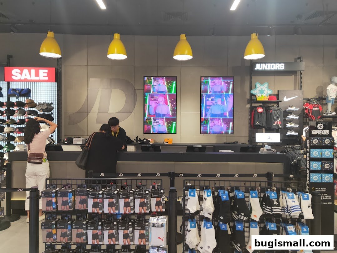 JD Sports store interior with a sale sign, display screens, and merchandise including socks and apparel.