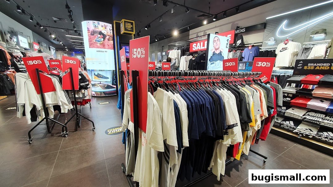 Interior view of JD Sports store with racks of t-shirts and sale signs.