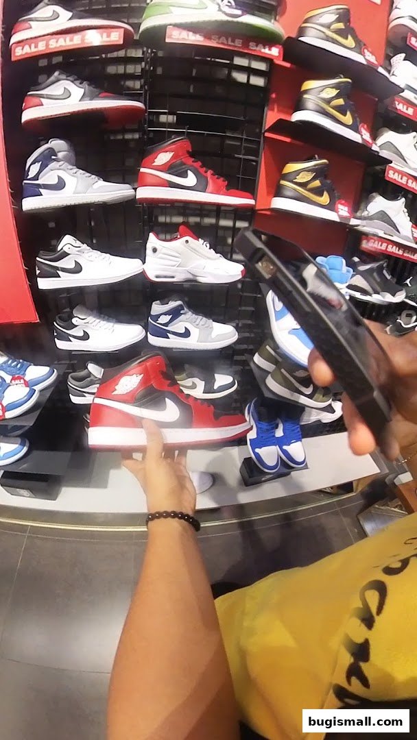 A person is holding a red and white sneaker in a JD Sports store with many shoes on display.
