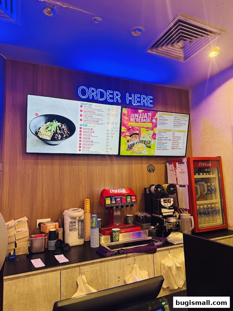 A counter area with digital menus, a Coca-Cola dispenser, and a refrigerator.