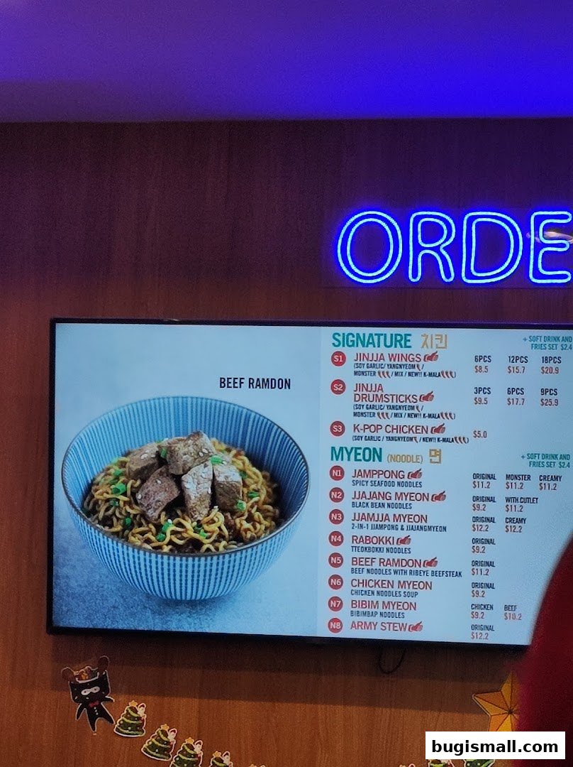 A digital menu board displaying Korean fried chicken and noodle dishes with prices.