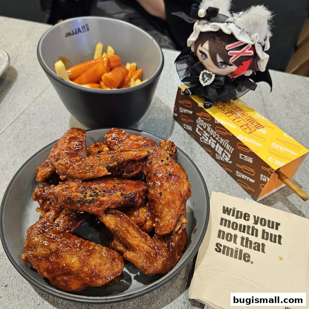 A plate of Korean fried chicken wings, tteokbokki, and fries with a JINJJA Chicken corn dog box.