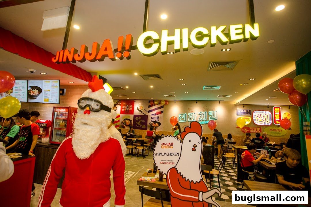 Interior of JINJJA Chicken restaurant with mascot, menu boards, and customers dining.