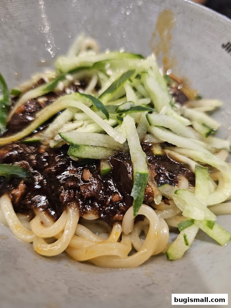 A close-up shot of JINJJA Chicken's signature noodles with savory sauce and fresh cucumber.