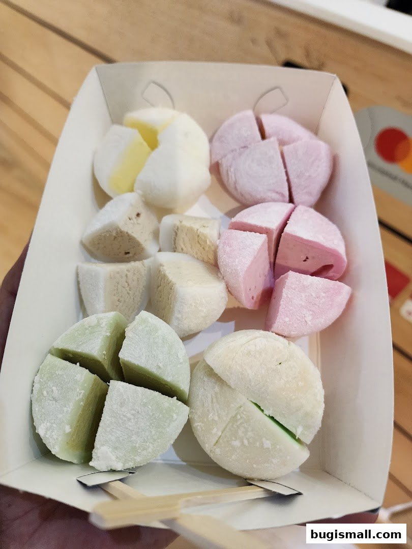 A hand holds a box of colorful mochi desserts, featuring various flavors and cuts.