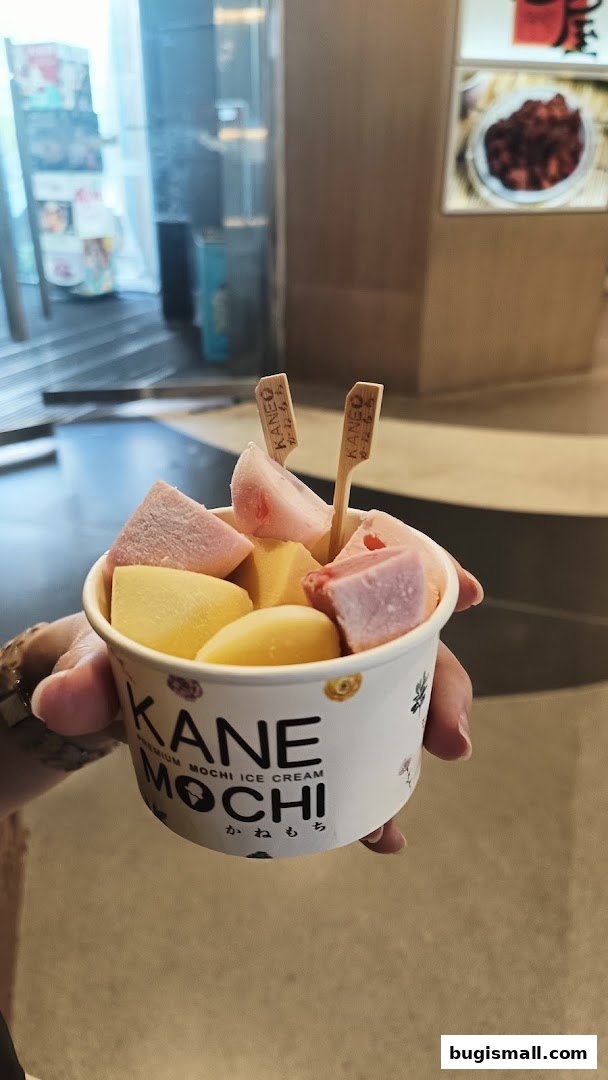 A hand holds a cup of colorful mochi ice cream with branded wooden sticks.