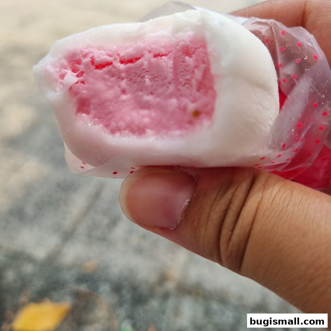 A close-up of a hand holding a strawberry mochi ice cream treat.
