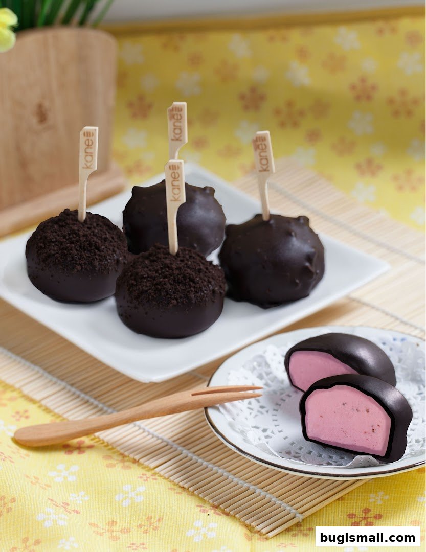 Delicious chocolate-covered mochi with cookie crumble and a pink filling, presented on plates.