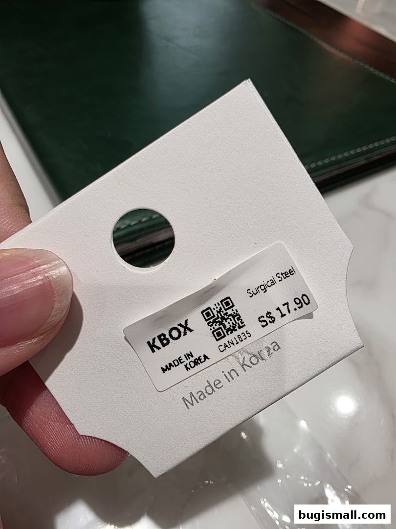 A hand holds a price tag for KBOX earrings made of surgical steel.