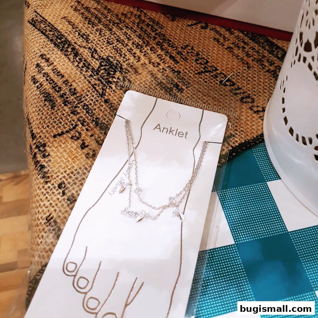A delicate silver anklet with sparkling charms displayed on a foot-shaped card.