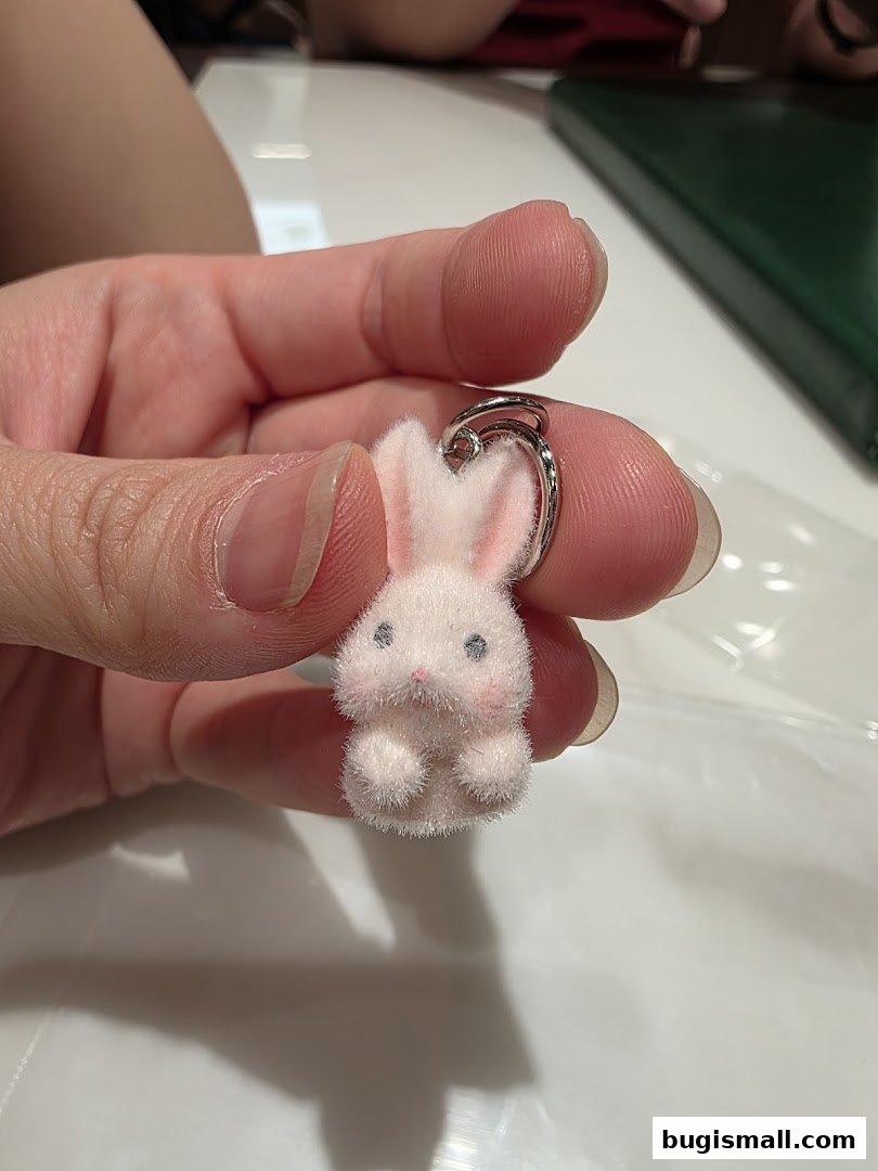 A hand holds a small, fluffy pink bunny charm with a silver ring.