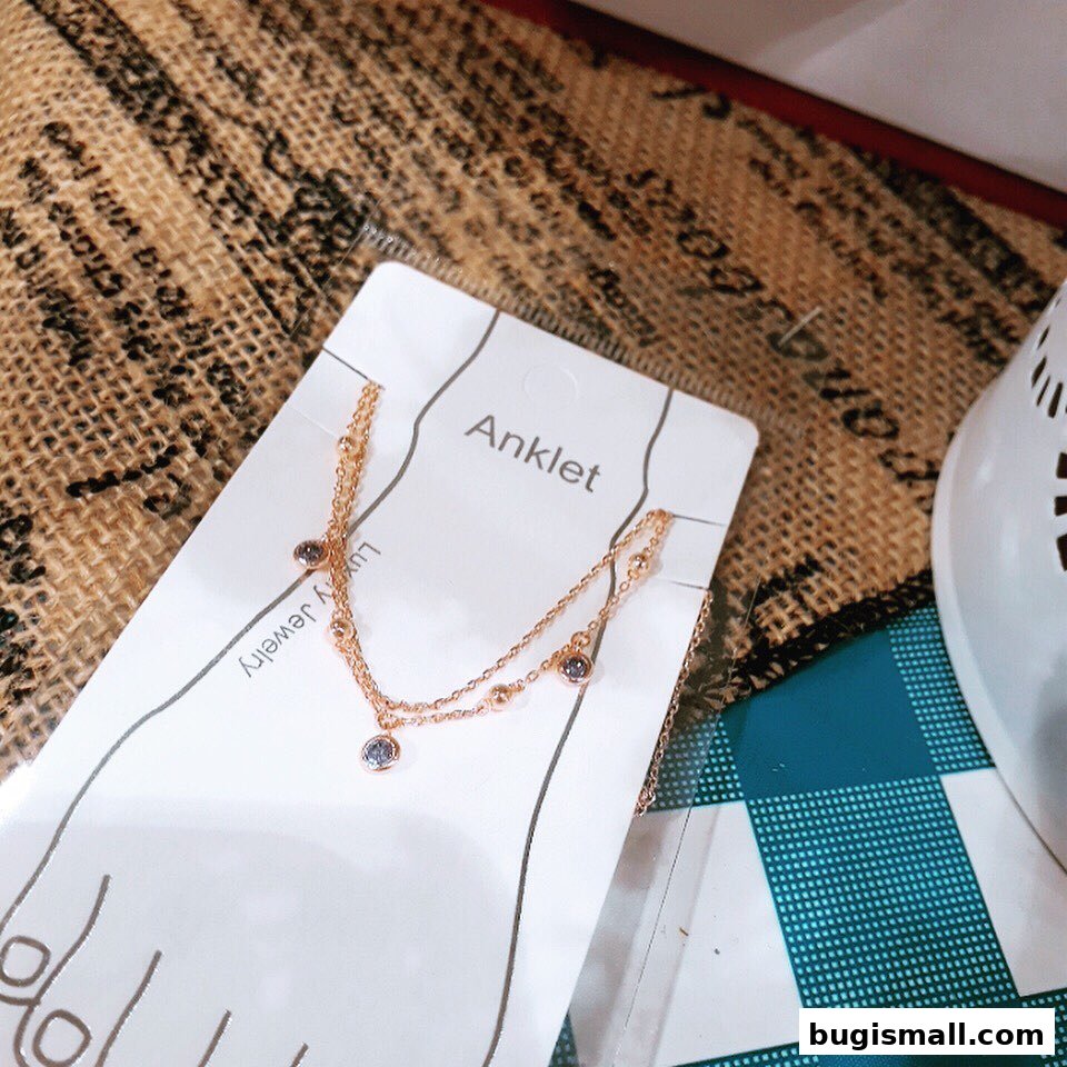 A delicate rose gold anklet with small blue stones on a white card.