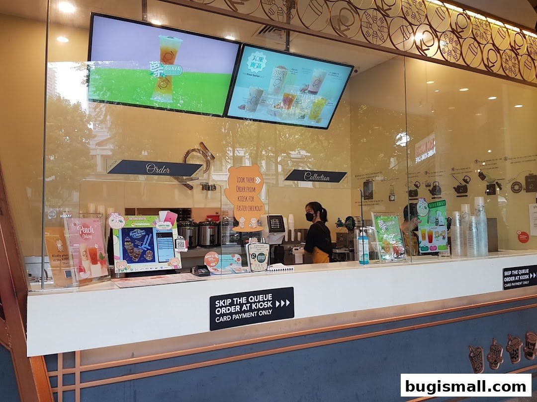 The KOI Thé Bugis shop counter with digital menus and a staff member serving customers.
